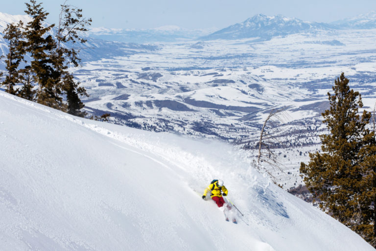 person in yellow jacket skiing off snowy mountain in eden utah - photo by doyouneedavacation