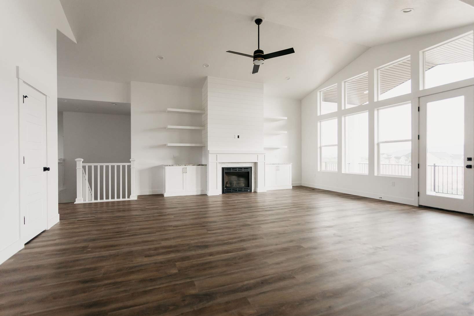 An open concept living room with large windows, a fireplace, wooden floors, and a white color scheme.