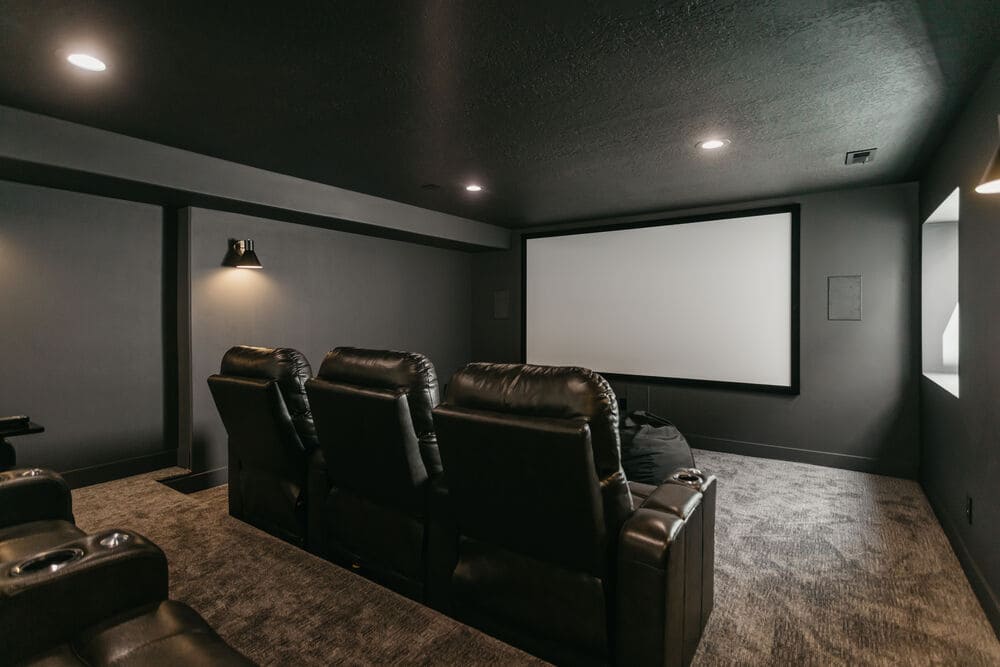 basement theater room with black walls and large projector screen and leather recliners by 10x builders in utah county